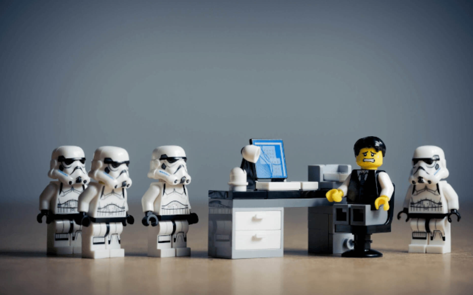 Star Wars Lego minifigures of storm troopers surround nervous office worker at a desk (metaphor for office power dynamics)